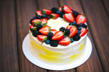 Birthday  lemon cake with strawberries, blueberries and blackberries on a dark wooden board