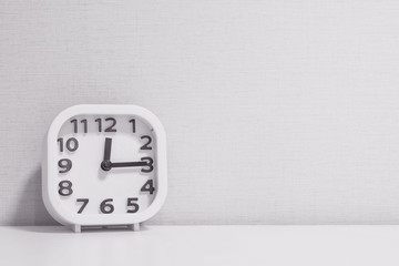 Closeup white clock for decorate show a quarter past twelve o'clock or 12:15 p.m. on white wood desk and cream wallpaper textured background in black and white tone with copy space