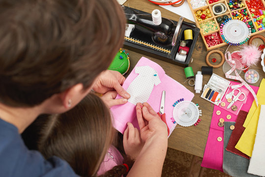 mother teaching daughter to sew doll clothes, top view, sewing accessories top view, seamstress workplace, many object for needlework, handmade and handicraft
