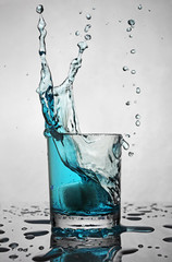 Splash in glass of blue alcoholic cocktail drink with ice cube