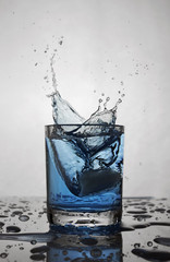 Splash in glass of blue alcoholic cocktail drink with ice cube