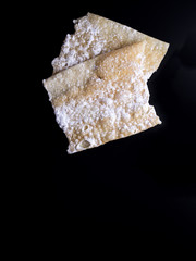 Oreillettes, french traditional pastry, sprinkled with powdered sugar and isolated on black background