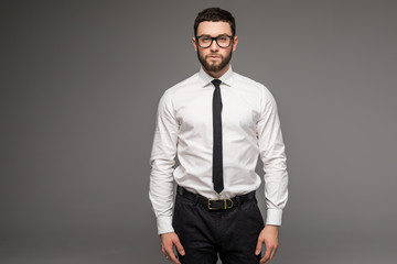 Handsome young businessman in white shirt and tie standing and glasses over grey background