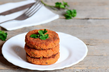 Home carrot cutlets on a plate and on a wooden table. Healthy fried carrot cutlets with green onions and parsley. Simple and quick vegetable cutlets recipe