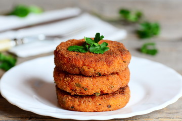 Homemade carrot cutlets on a plate. Delicious fried carrot cutlets with green onions and parsley. Healthy meatless cutlets recipe. Closeup