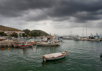 Fototapeta na wymiar Fishing boats in small harbour under a rainy cloudscape