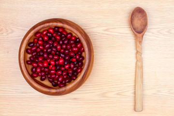 Healthy food. Wooden plate with fresh cornel in it and wooden spoon isolated on beige background. 