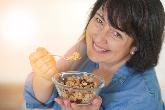 Dark-haired woman in kitchen eating cereals