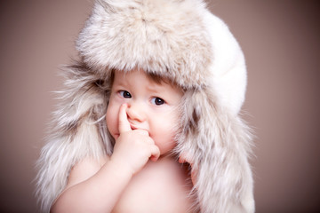 Baby in a huge fur hat doubts, propping his face with his hand