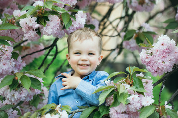 Cute baby boy among pink blossoming flowers