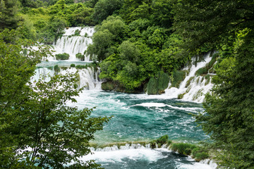 Fototapeta na wymiar Foamy waterfall rapids falling down by cascades of waterfall Skradinski Buk on a sunny day. Krka National Park, Croatia.