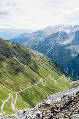 Alp road surrounded by blue alp high mountains and green hills. Steep descent of Passo dello Stelvio in Stelvio Natural Park, Tyrol, Italy.