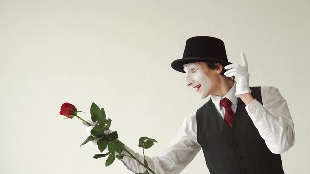 Man mime with a red rose on a white background. He plays with a flower and gives it to someone