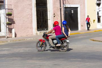 Obraz na płótnie Canvas Man and a woman is riding a vintage scooter in the streets of Mexico. Slight motion blur effect 