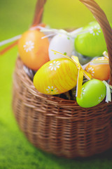 Colored Easter eggs in a wicker basket on a green background.