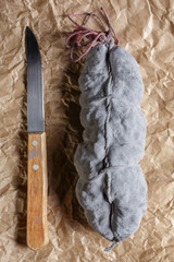 Sausage salami and knife on beige paper top and side view. Sausage sausage with ashes. French country sausage. Rustic food still life