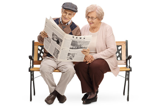 Seniors sitting on a bench and reading a newspaper together