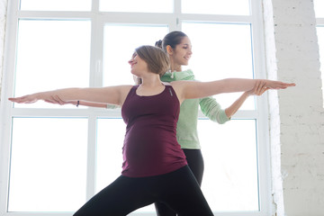 Fototapeta na wymiar Yoga trainer assisting pregnant woman while doing exercises
