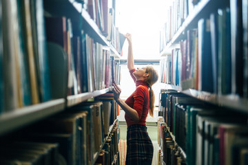 Young librarian searching books and taking one book from library bookshelf