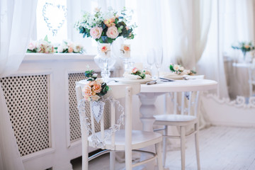 Interior design of white room with beautiful flowers on the served table. Big windows and creative classical mirror at the background. Horizontal