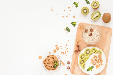Healthy breakfast with yogurt, muesli, fresh green fruits, cereal, nuts on white background. Flat lay, top view.