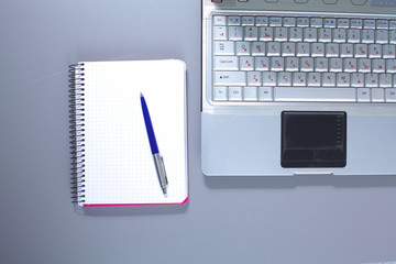 A note book, laptop, pen, graph paper document on the office desk table behind white blind