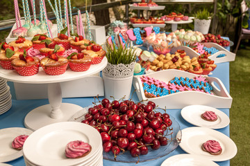 Seven little kids sit at red table with cake and throw confetti at birthday party. Inscription Happy Birthday on wall