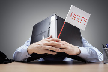 Businessman burying his head uner a laptop asking for help - 141874763