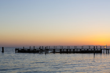 Obraz premium Beautiful sunrise on a wooden pier in the shores of Caribbean sea. Silent beach. Peaceful. Sun is rising behind the silhouette dock.