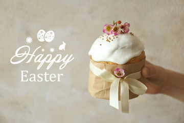 Hand holding Easter cake decorated with ribbon and flowers on light background
