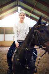 Blonde?concentrated female sitting astride dark horse