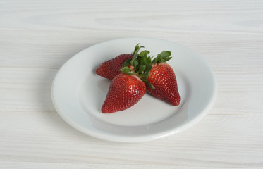 Fresas en un plato en mesa de madera blanca y pared azul