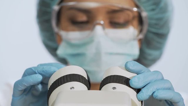 Biracial female researcher adjusting microscope lenses, conducting research
