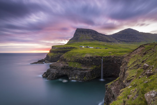Gasadalur, Vagar island, Faroe Islands, Denmark. The iconic waterfall jumping from the cliff into the ocean at sunset.