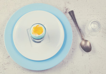 blue easter egg with yellow yolk, spoon, top view on wooden aged table - easter breakfast concept, retro toned