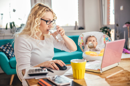 Mother drinking water while using laptop office