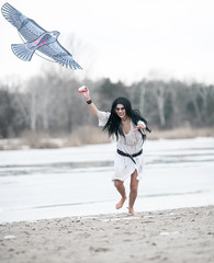 Crazy young woman runs on sand along lake with kite in her hand.