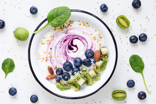 Smoothie Bowl With Acai Berry, Kiwi, Blueberries, Almonds, Coconut, Bee Pollen And Baby Spinach On White Background. Top View Of Healthy Detox Smoothy Bowl