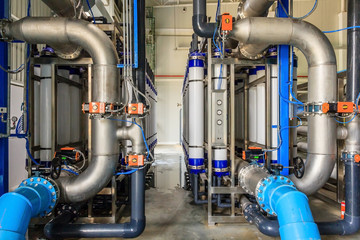 Large industrial water treatment and boiler room. Shiny steel metal pipes and blue pumps and valves.