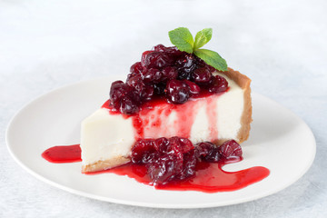 Cheesecake with sour cherry sauce and mint leaf on white plate