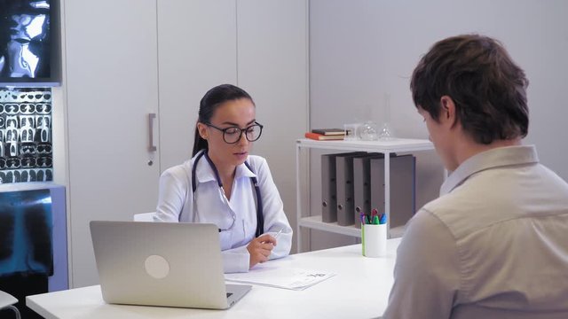 Doctor informs patient bad news. Professional md sitting in the office wearing in white coat. Opposite woman sit man his face we cannot see.