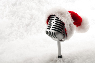 Carols and Christmas music concept with a microphone wearing a santa hat isolated on white snow...