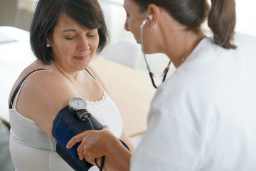 Obraz premium Mature woman at the doctor, controlling blood pressure