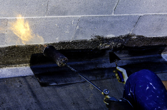 Roofer installing rolls of bituminous waterproofing membrane for the waterproofing of a terrace