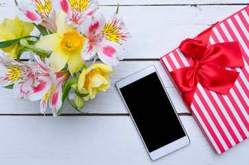 Spring composition: bright flowers and a smartphone on a wooden table.