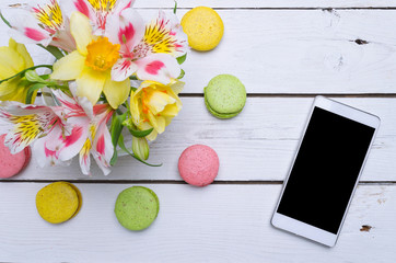 Spring composition: bright colors, multicolored macaroons and smartphone on a wooden table.