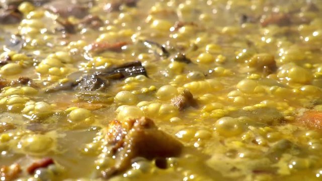 Cooking authentic Valencian paella with chicken meat, rabbit meat, vegetables, boiling Valencian rice, saffron. Typical cuisine of the Valencia Spain. Boiled bubbles in slow motion