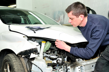 Mechanic inspecting car body damage at auto repair shop service station.