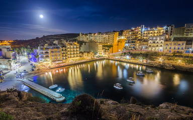 Fototapeta na wymiar Xlendi, Gozo - Night photograph of Malta's most beautiful mediterranean town with busy night life, restaurants, hotels and moon light on the island of Gozo