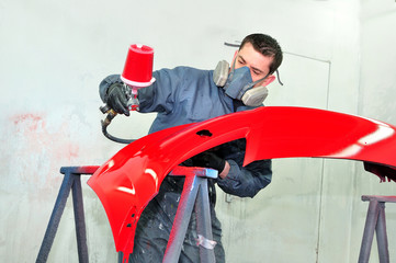 Worker painting red car bumper.